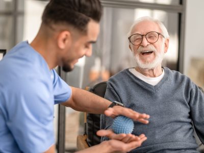 Joyous aged man undergoing a session of physical therapy conducted by an experienced rehabilitation doctor